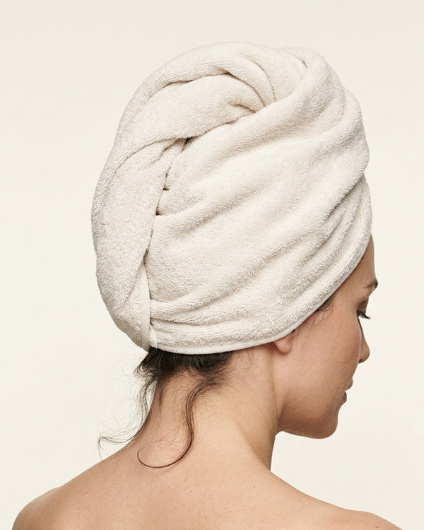 Woman with hair wrapped in a cream towel during a castor oil hair ritual