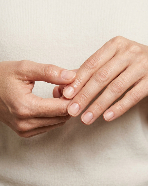 Hands massaging castor oil into the cuticles of bare, natural nails