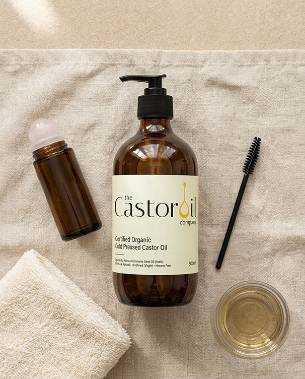 Certified organic castor oil in a 500ml amber glass bottle with pump, beside a rose quartz roll-on
