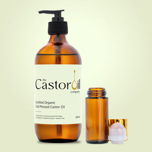 Certified organic cold-pressed castor oil, 500ml amber glass bottle with pump dispenser, beside a rose quartz roll-on bottle with gold cap